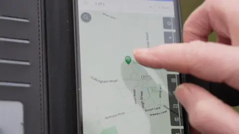 A close up of a mobile phone screen. The screen shows a map with a green location icon on it. A finger is about to press this location icon.