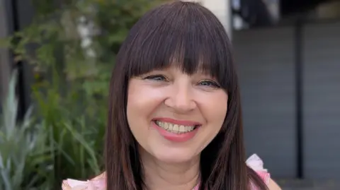 Tanya smiles at camera, wearing a pink top