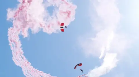 A parachuter and red smoke falling through the sky