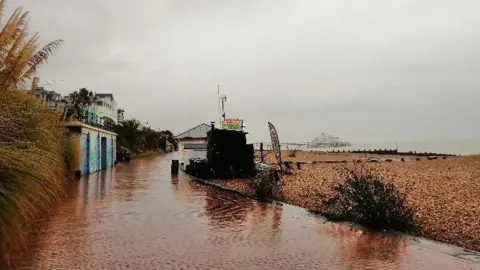 Janasis Eastbourne seafront on a rainy day. A paved path, the beach and the sea are visible. 