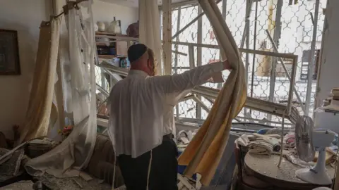 AFP A man inspects an apartment which was damaged by a rocket fired by Hezbollah from Lebanon, in Kiryat Yam, near Israel's northern city of Haifa (8 October 2024)