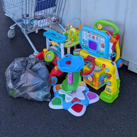 Enfys Foundation Children toys and a black bin bag left on the car park floor outside charity shop