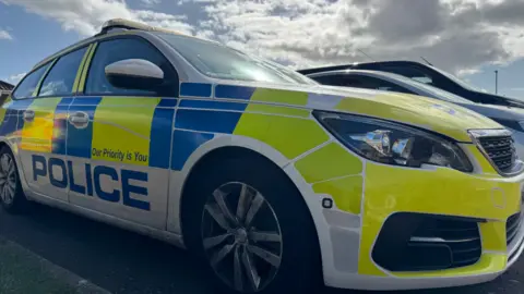 The side of a police car, with yellow and blue reflective livery.