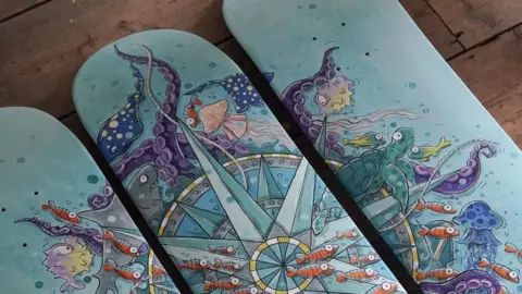 Zoe Sadler Nautical Compass by Zoe Sadler - three skateboard decks painted with a nautical theme with a compass, jellyfish and orange fish.