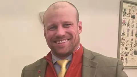 NFU Oliver Collingham wearing a suit and yellow tie