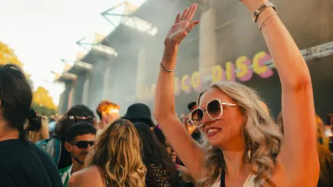 Here and Now A woman wearing a white top and sunglasses waves her arms during an Alfresco Disco event in Bristol