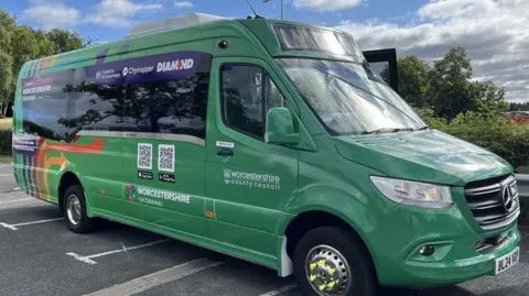 A green Mercedes minibus parked in a car park, side on. It has darkened windows and various words written on it including "Worcestershire County Council".