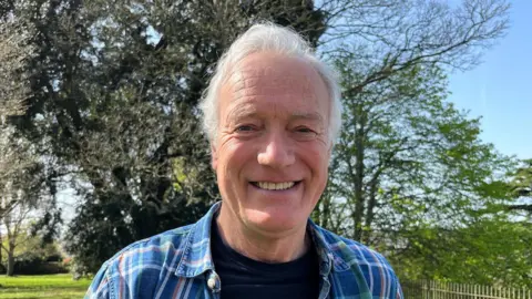 Gerry Shattock - a man with grey hair wearing a blue checked shirt and a navy T-shirt