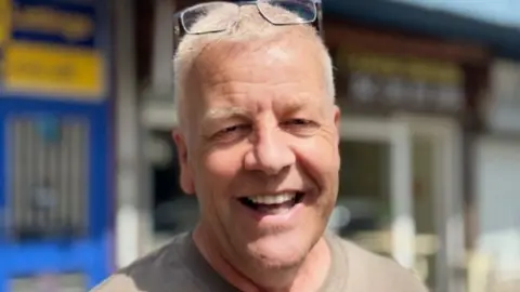 Gemma Dillon/BBC Kevin Lobley smiling, has glasses on head, grey hair and grey top