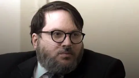 Bbc the beard of the beard and oxygen tube on his nose. He wear glasses and dark coats