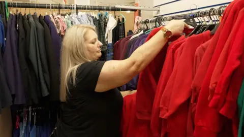 BBC Michaela Wilson looks through a rack of children's school uniforms