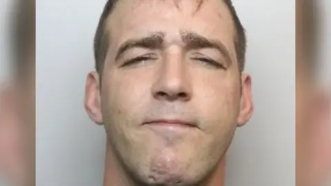 A police mugshot of Michael Stewart. He has short, dark hair.