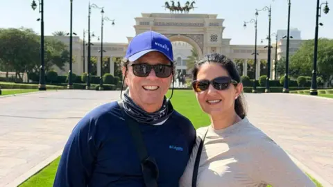 Krista Jucknath Hickman and her husband Mike, both in sunglasses, pose for a photo in front of a decorative archway in Dubai