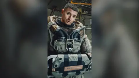 A still from a computer game showing a man with short dark hair in heavy-duty armour.