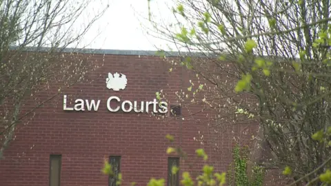 The outside of Bodmin magistrates court. The words Law Courts are displayed in silver on a solid brick wall. There are trees and branches in front of the building. 