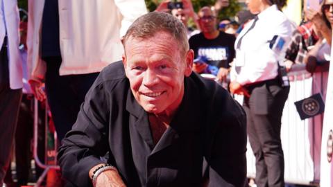 A picture of Ali Campbell smiling and wearing a black shirt