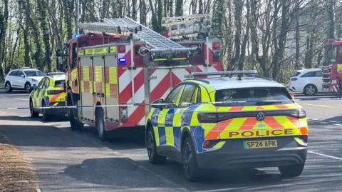 PA Media a police car which has bright yellow, blue and orange panelling parked behind a a red fire engine