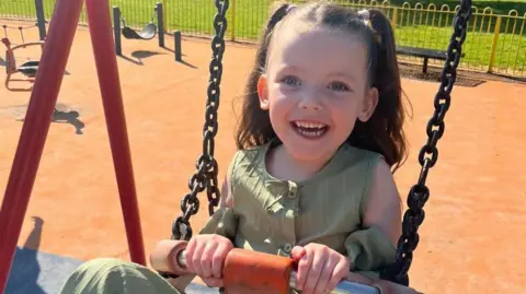 BBC Niamh je fotografován na houpačce v Playparku. Má vlasy ve dvou copáncích po stranách, které drží na místě růžovými luky. Usmívá se. Má modré oči a má na sobě zelený vrchol.