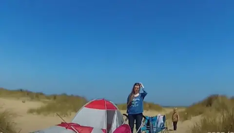 Suffolk Police/Norfolk Police Video grab of a woman and a young child next to a tent on a beach. The woman is wearing a blue top. The child is in the background wearing a brown top and leggings. 