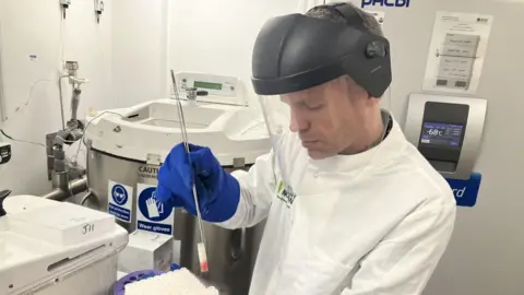 Dr Thomas Turner wearing protective laboratory clothing handling one of thousands of research samples 