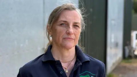 A woman with blonde hair is standing outside wearing a blue T-Shirt
