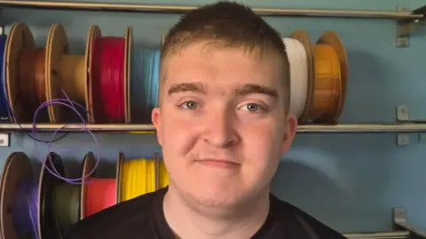 A 17-year old boy with brown hair smiling at the camera with wires behind him.