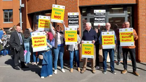 Nadia Lincoln/LDRS A large group of people holding up banners outside a council building. They are all looking in different directions. 