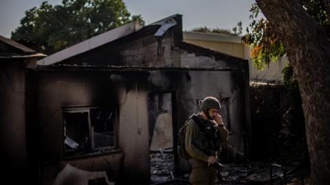 An Israeli soldier stands next to a damaged house in Kibbutz Be'eri, southern Israel (14 October 2023)