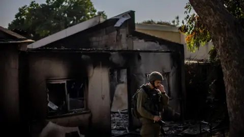 EPA An Israeli soldier stands next to a damaged house in Kibbutz Be'eri, southern Israel (14 October 2023)