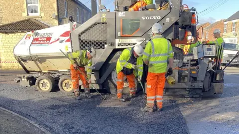 A group of three men resurfacing Ladyfield Road. There is a large vehicle behind them. All are wearing protective gear.