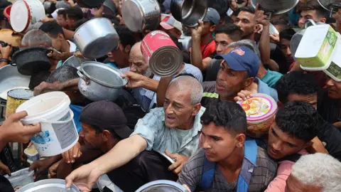 AFP Palestinians wait for food at a community kitchen in Nuseirat, in the central Gaza Strip (11 June 2025)