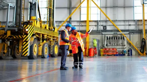 Two men in blue hard hats stand in a warehouse