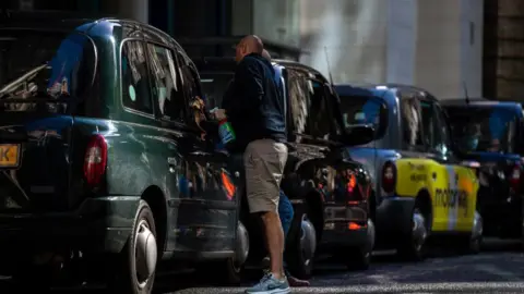 Getty Images Taxi driver cleans window whilst waiting at a taxi rank