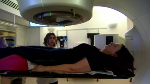 A woman lies on a radiotherapy machine bed.