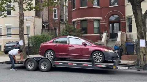 Um carro vermelho com uma janela esmagada está em um trailer