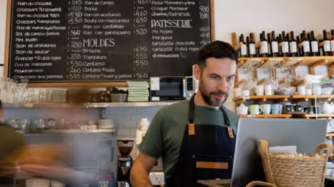 Getty Images A barista looking in to laptop with a menu and food items behind him