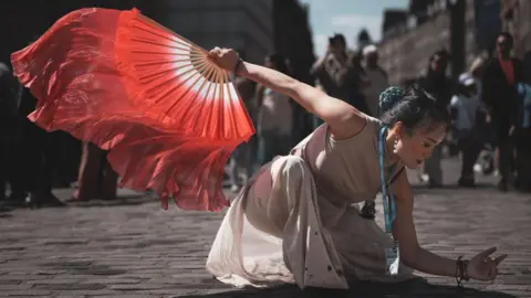 Gordy Macdonald Woman performing in street with red fan during the Edinburgh Fringe Festival.