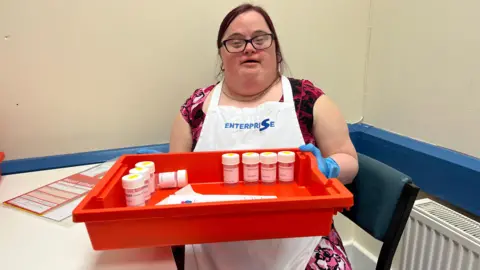 Becky from Enterprise Packaging holding a tray used to sort components for transplant retrieval kits, including sealed pots and sheets of paper.