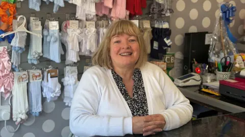 A woman smiles from behind shop counter 