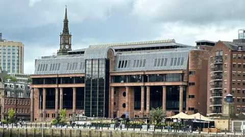 Newcastle Crown Court is an imposing building made from smooth red stone with massive black windows and tall columns along its frontage.