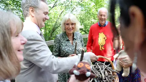 PA Media Queen Camilla, Patron of the Royal Literary Fund, and Gyles Brandreth (right) play a game of pooh sticks on Poohsticks Bridge during a visit to Ashdown Forest, to commemorate 100 years since the publication of the first Winnie the Pooh book in 1926. Ashdown Forest was the inspiration for the original Hundred Acre Wood and former home of author, A A Milne.