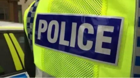 Close-up picture of a police jacket, featuring a blue section bearing the words 'police' on top of a yellow high-vis section.