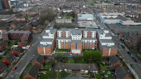 Image is from drone footage of Queensland Place in Liverpool. It is a five-storey block of student accommodation, with two central buildings and wings on other side, surrounded by private residential accommodation, mainly bungalows. 