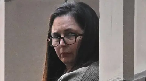Erin Patterson wearing glasses and a grey knit top looks at the camera