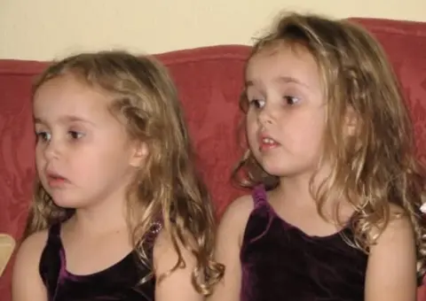 PA Media Caitlin and Grace at around four years old. They have blonde hair and both wear purple tops. They look extremely similar. 