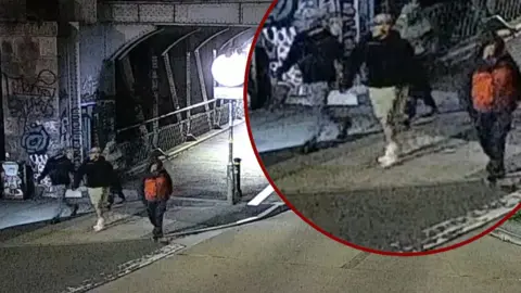 Avon & Somerset Police Grainy CCTV footage of four men walking along a road after coming off a footbridge. One is wearing a distinctive black and orange hooded coat.