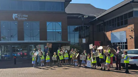 Pupils and teachers outside the council building wearing yellow hi-vis jackets and holding placards. 