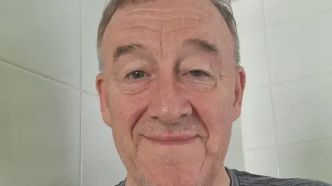 Donald McColgan Donald McColgan, who has short grey hair. There are white tiles in the background behind him.