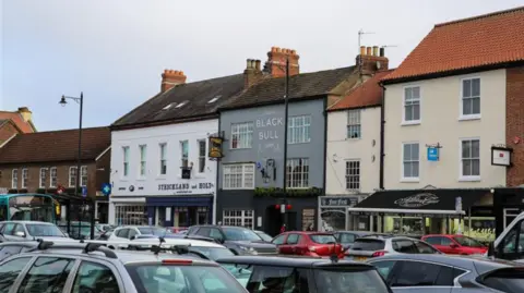 A view of Yarm High Street with the pub the Black Bull in the middle of the picture. The roofs of lots of parked cars can be seen at the bottom.