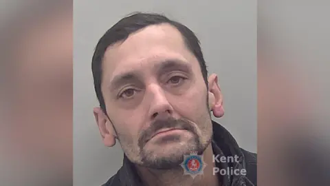 Kent Police A man with dark hair and beard, and wearing a dark jacket.